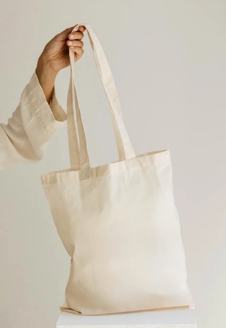 A plain cotton tote held up by its handles, being screen printed with a logo